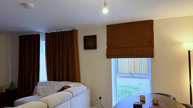 Open-plan living and dining space with a Roman blind over the window and curtains at the patio door.