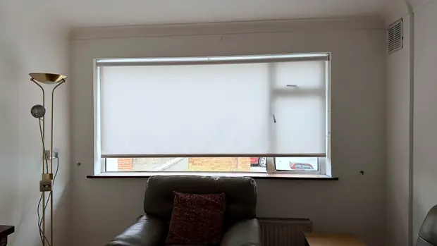 Sitting room with a cream blackout roller blind pulled halfway down a wide window.
